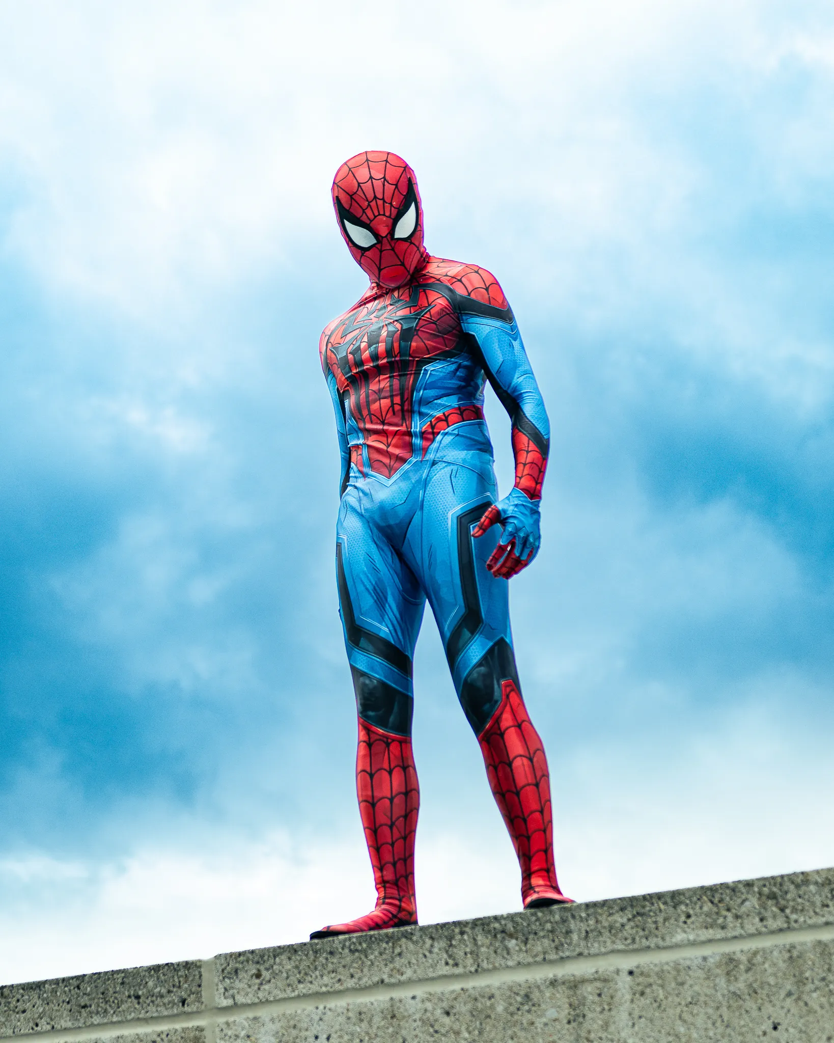 A cosplayer featuring spidermam perching on top of a concrete platform.